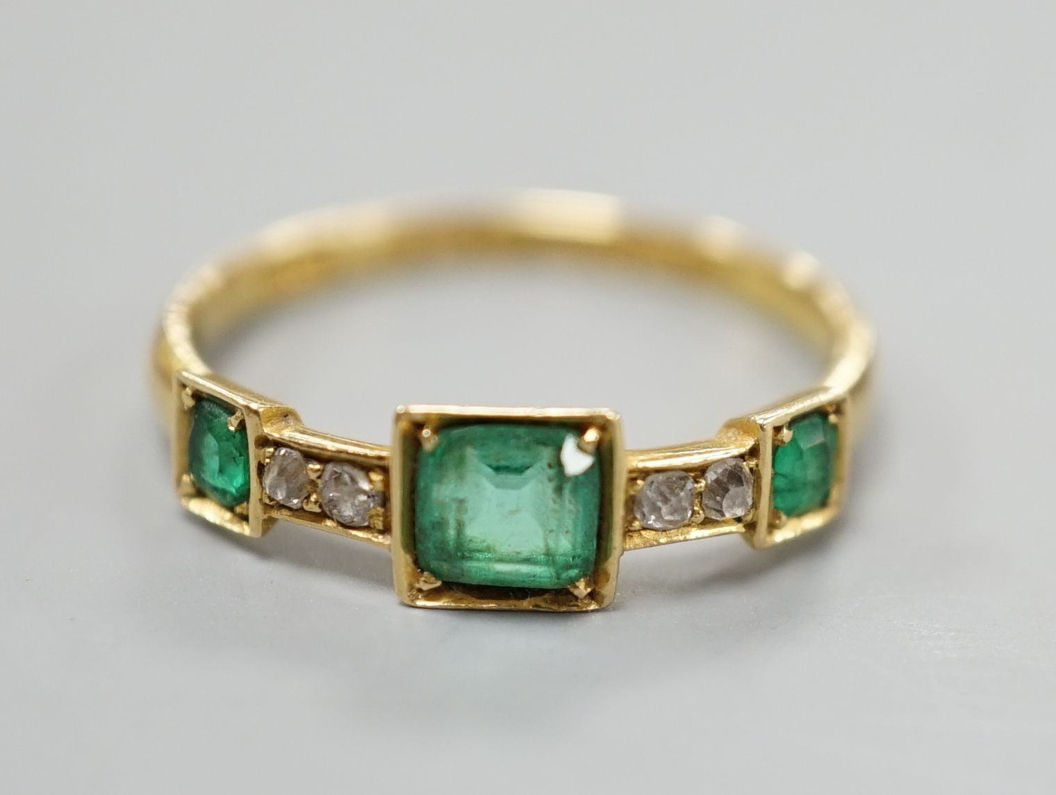 A George V 18ct gold, three stone emerald and four stone diamond chip set half hoop ring, size L, gross weight 1.8 grams.